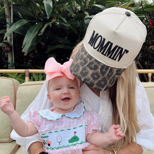 Woman holding a baby wearing a pink outfit with a large bow, sitting outdoors.