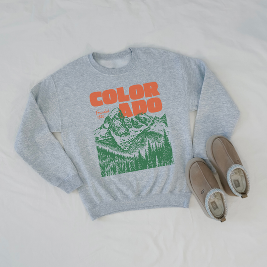 Gray sweatshirt with 'COLORADO' and mountain graphic, paired with brown slippers on a light gray background