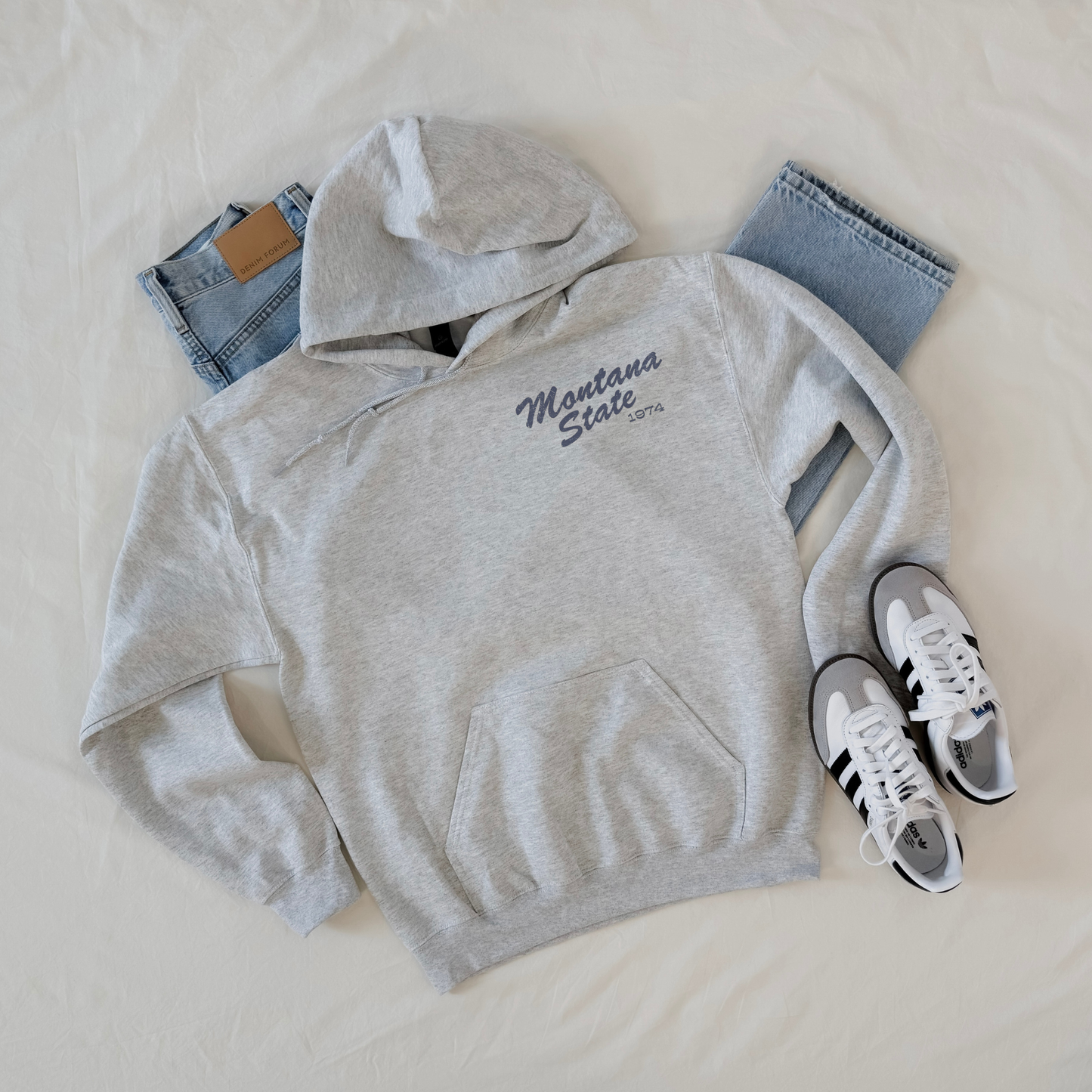 Gray hoodie with 'Montana State' text, jeans, and sneakers on a light background