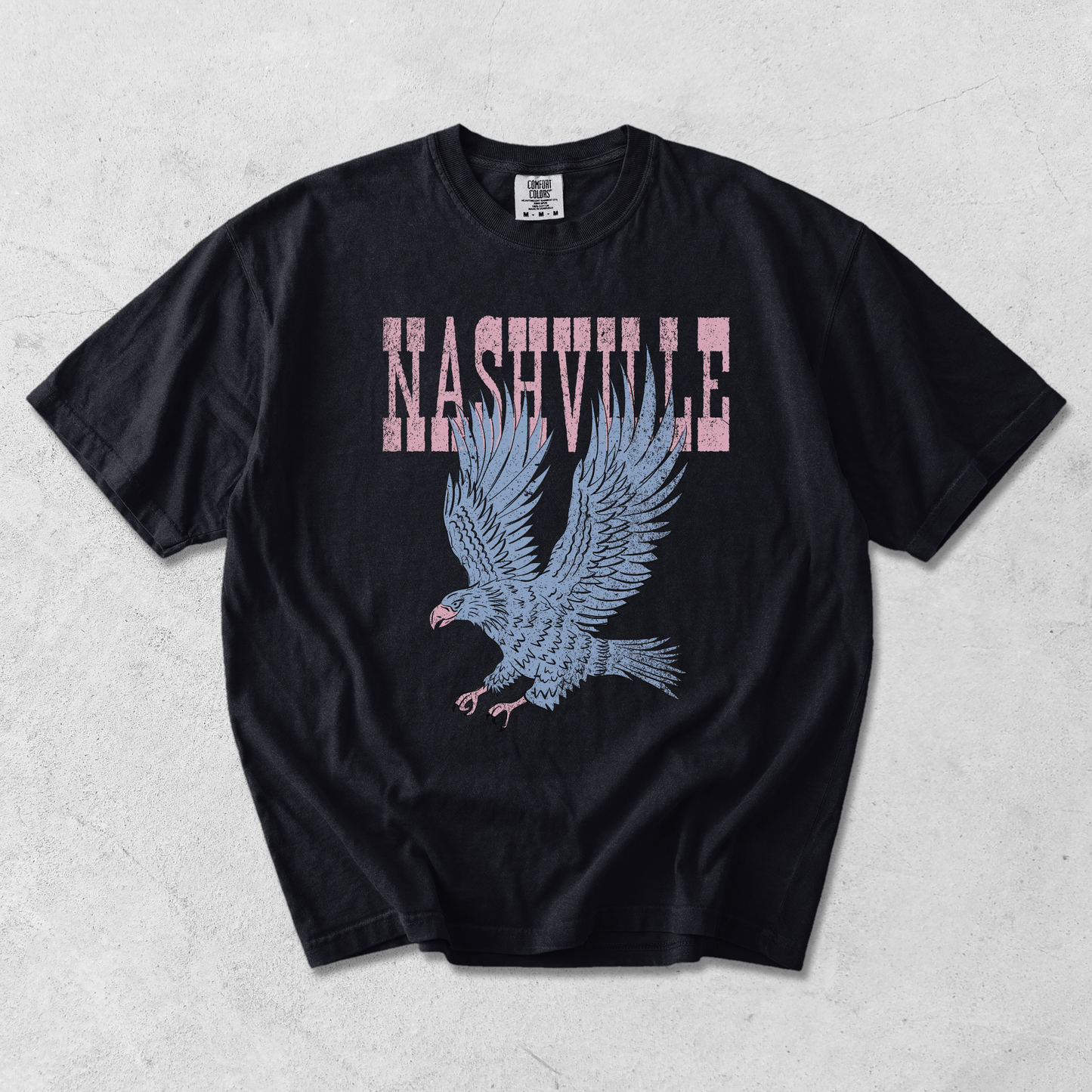 Black Comfort Colors Nashville graphic tee with distressed pink lettering and vintage blue eagle graphic on textured background.