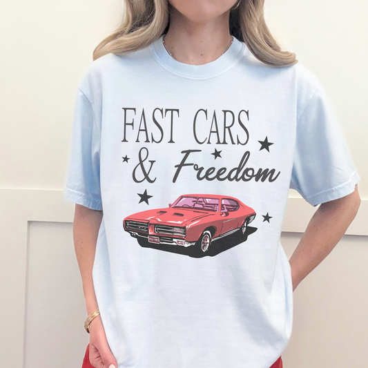Chambray blue Fast Cars & Freedom t-shirt with retro red muscle car graphic and black star accents styled casually.