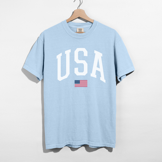 Chambray blue USA varsity graphic tee with white lettering and American flag detail hanging on wooden hanger