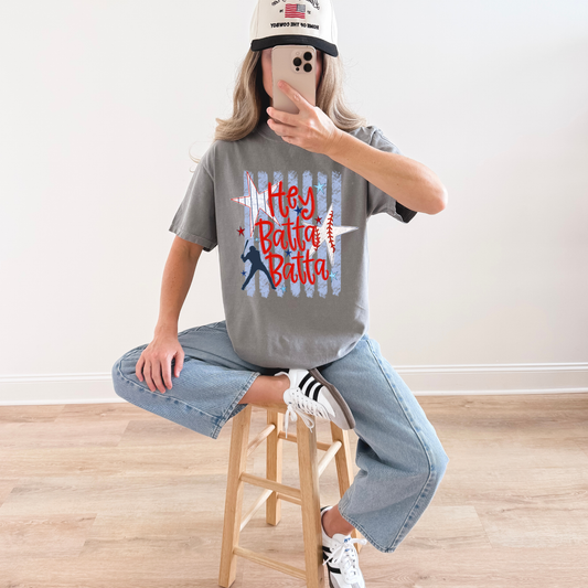Woman wearing grey vintage baseball graphic t-shirt with red white and blue design styled with jeans and sneakers indoors.