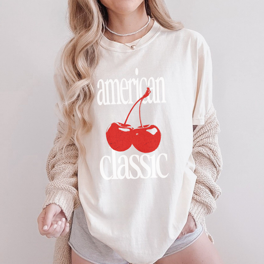Woman wearing ivory ‘American Classic’ cherry graphic tee styled with cardigan and shorts