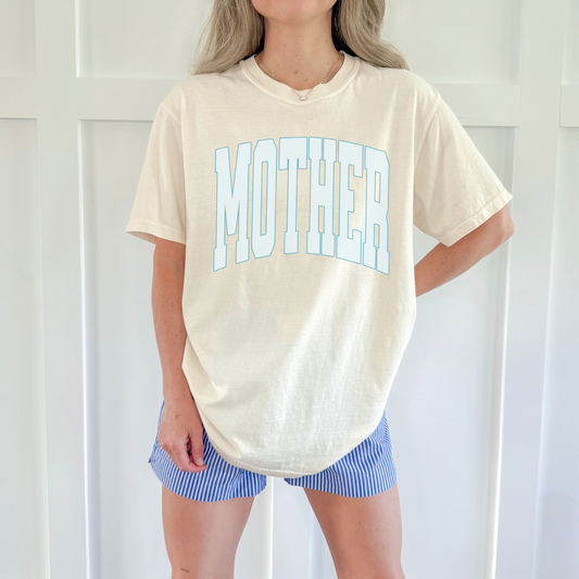 Relaxed fit ivory graphic tee with “MOTHER” design, styled with striped shorts for everyday wear