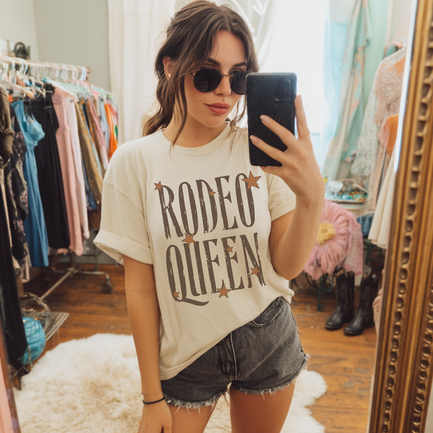 Woman wearing Rodeo Queen western graphic tee styled with denim shorts and sunglasses in boutique setting
