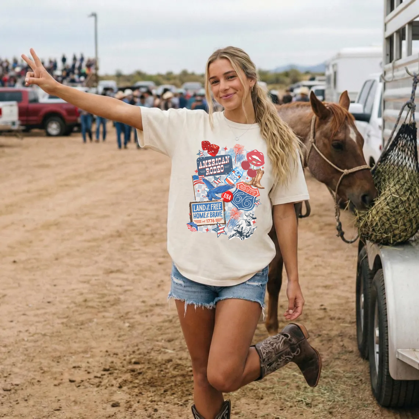 Ivory patriotic western graphic tee with American Rodeo Route 66 collage design worn with boots and shorts next to a horse at a rodeo event.