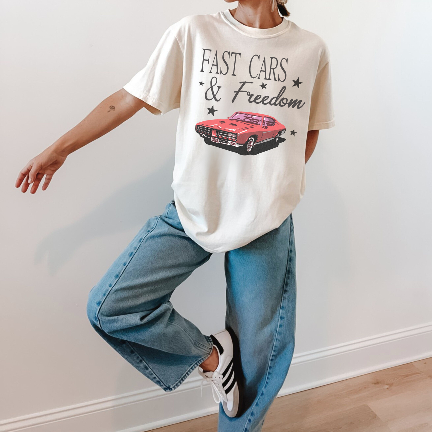 Ivory vintage Americana graphic tee with red muscle car and Fast Cars & Freedom text styled with relaxed denim jeans and sneakers.