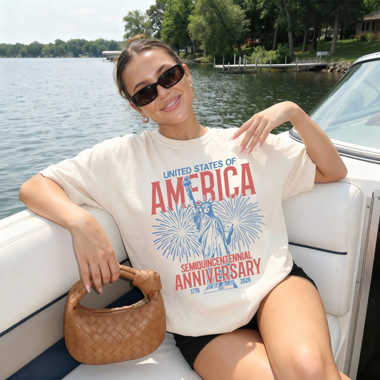 Woman wearing ivory America 250th anniversary patriotic graphic tee on boat with Statue of Liberty fireworks design
