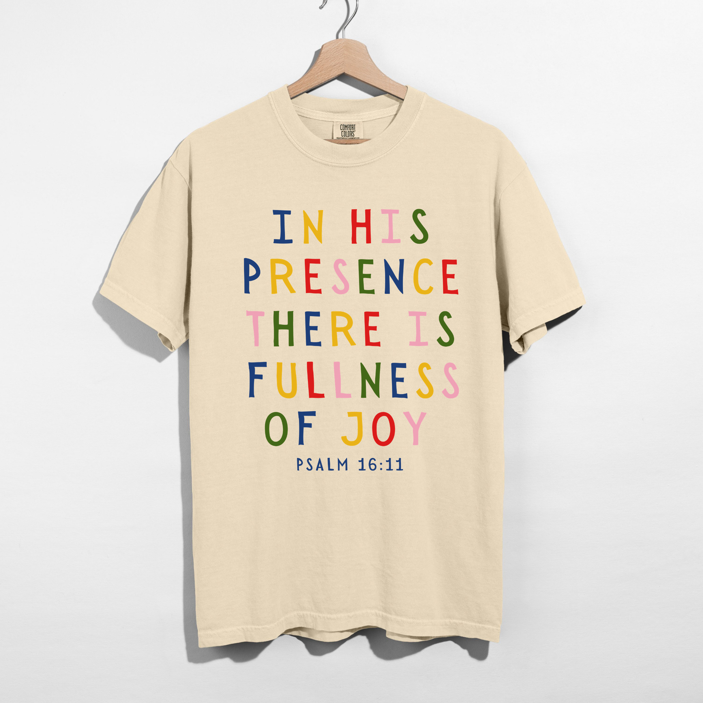 Ivory Christian graphic tee displaying the colorful Psalm 16:11 Bible verse In His Presence There Is Fullness of Joy on a premium garment-dyed unisex shirt.