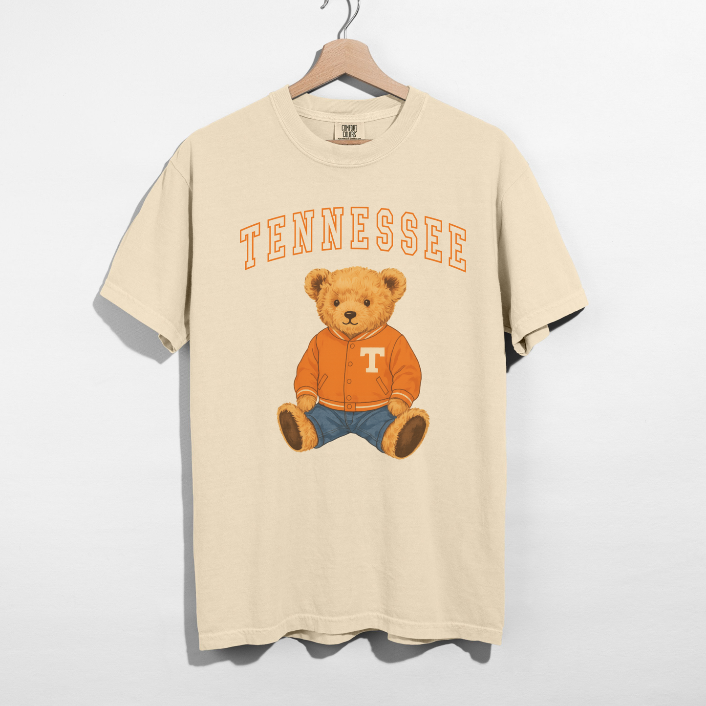 Updated Tennessee teddy bear graphic tee featuring a vintage collegiate Tennessee arch and adorable teddy bear wearing an orange varsity jacket on an ivory heavyweight cotton t-shirt.