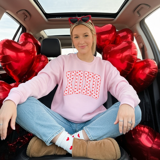 Model wearing light pink XO heart print Valentine crewneck sweatshirt sitting in car with red heart balloons