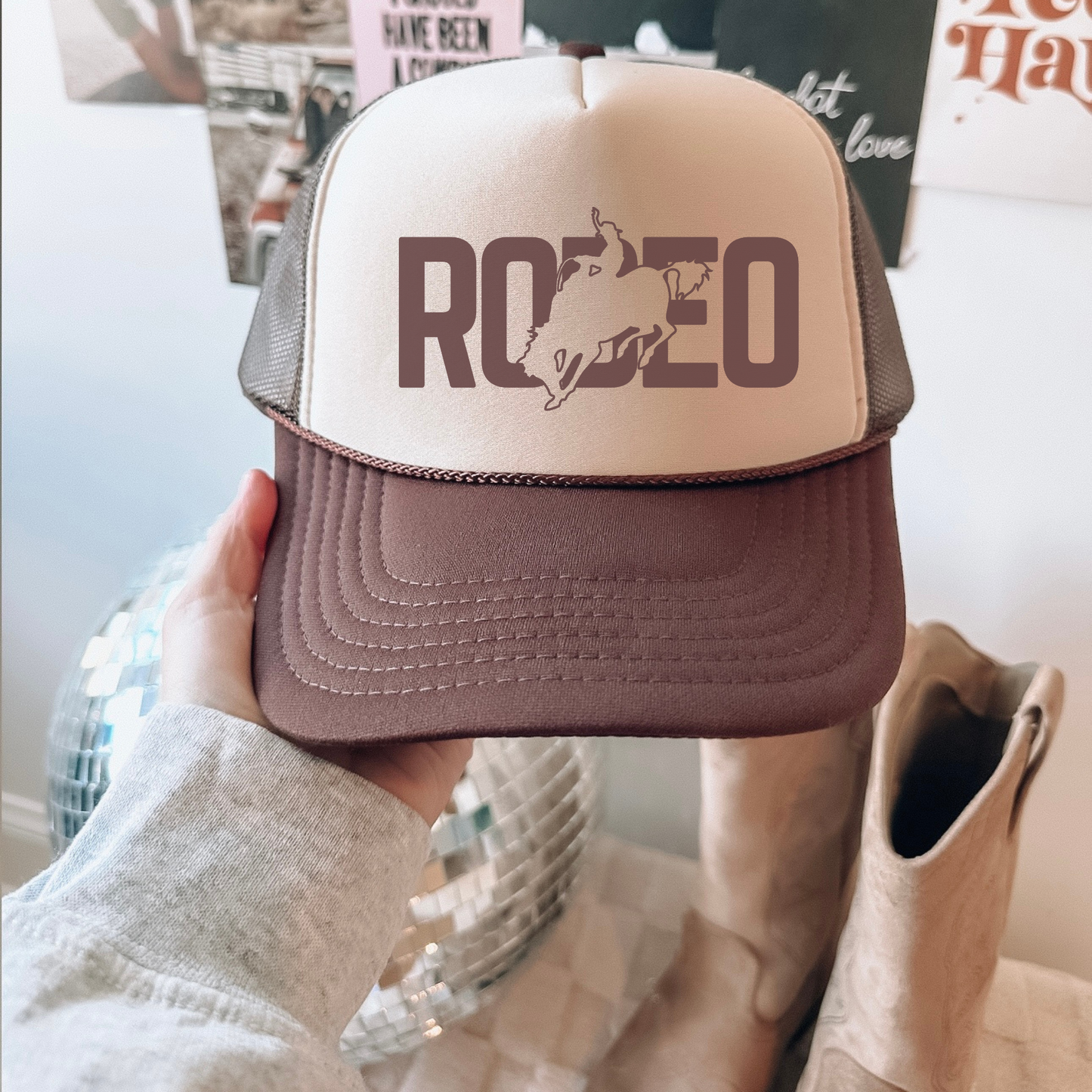 Trucker hat with 'RODEO' and horse graphic held by a person wearing a light gray sweater.