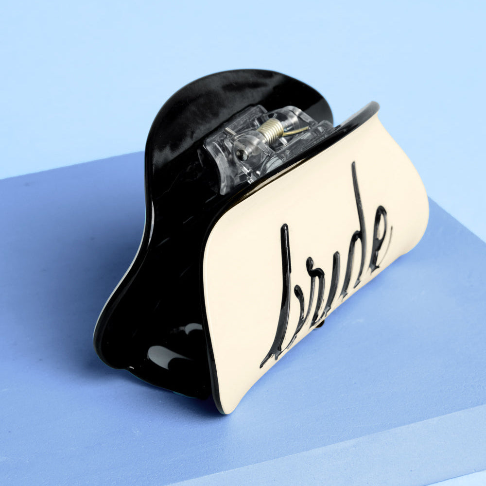 Ivory bride claw clip with black recessed logo on blue background close-up detail