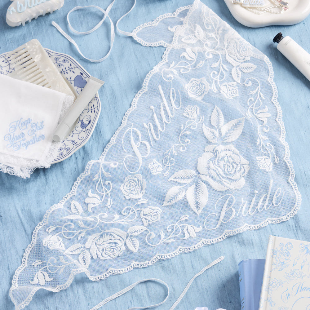 Lace head scarf with 'Bride' embroidery on a blue surface with decorative items.