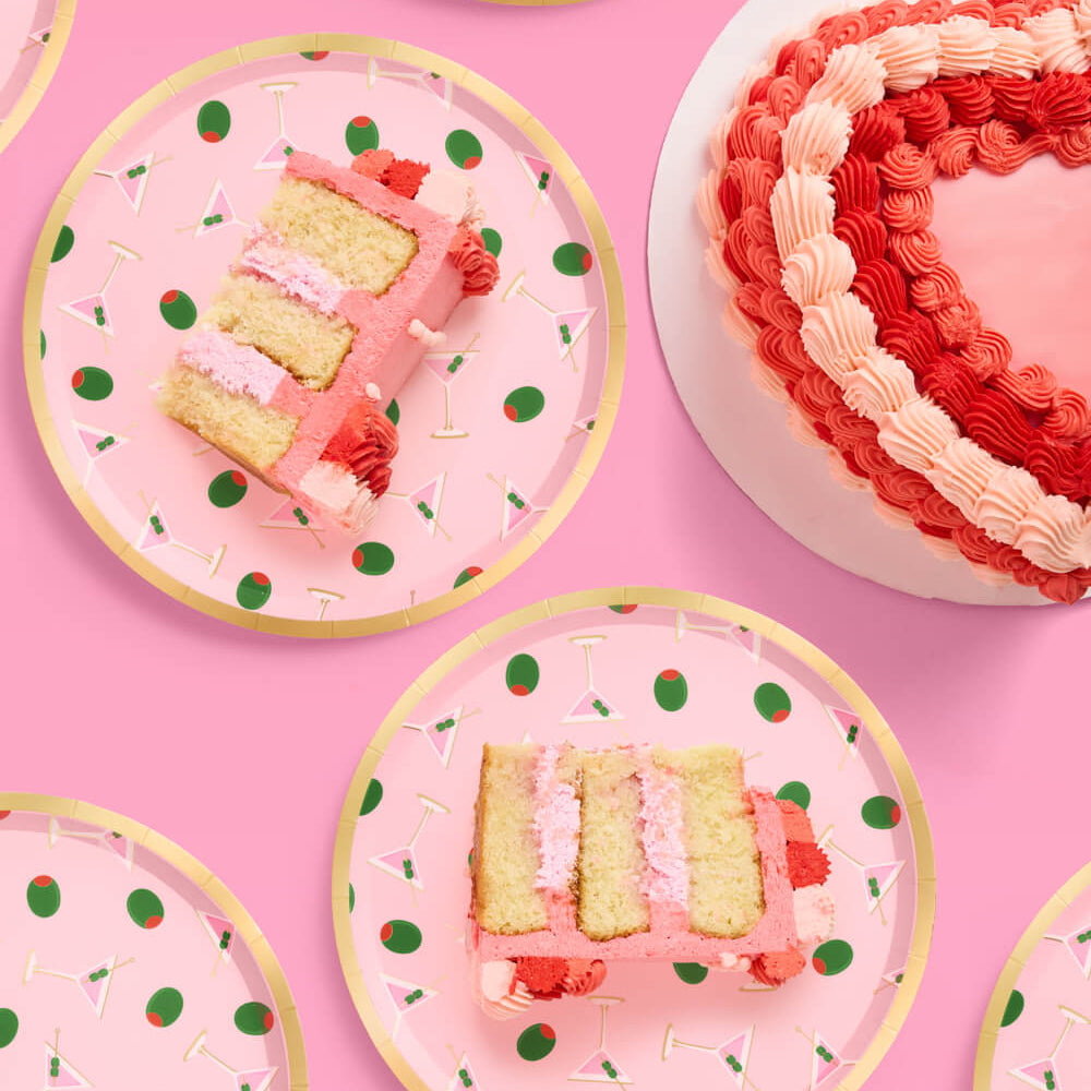 Pink martini party plates with gold foil details styled with cocktails and olives with slices of cake