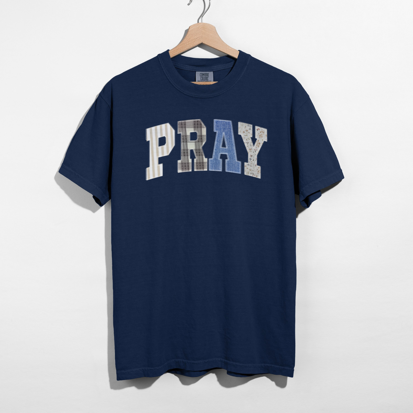 Navy blue t-shirt with 'PRAY' printed on it, hanging on a wooden hanger against a white background.