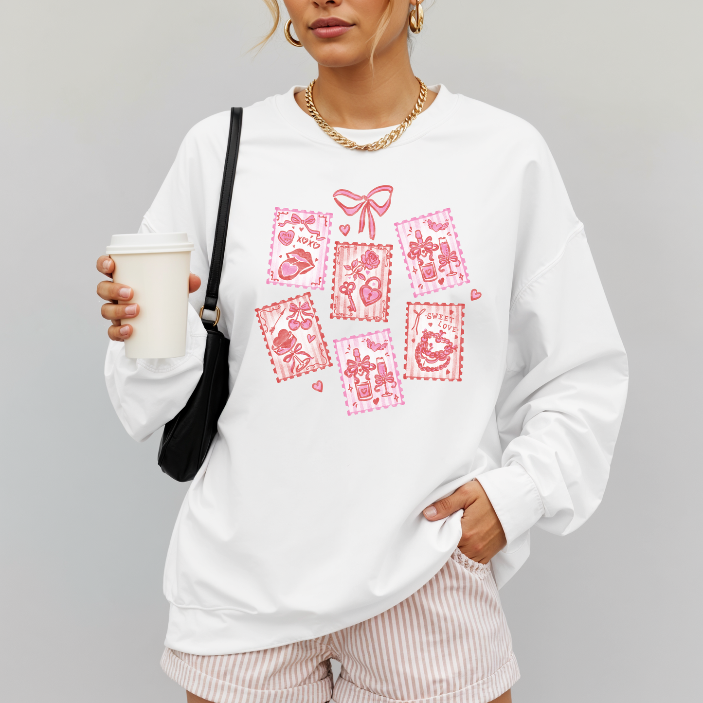 Woman wearing white Valentine stamps sweatshirt with pink hand-drawn graphic, holding coffee.