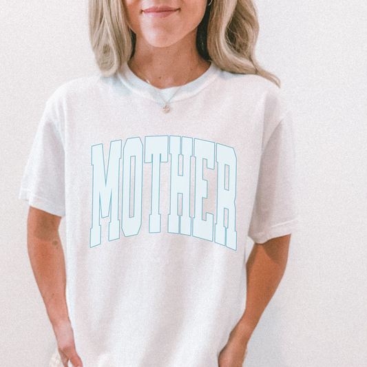 White unisex graphic tee featuring arched “MOTHER” lettering in light blue, styled casually on model