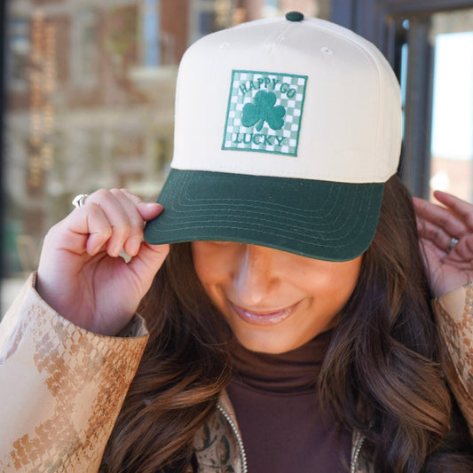 Person wearing a white and green cap with a shamrock design, outdoors.