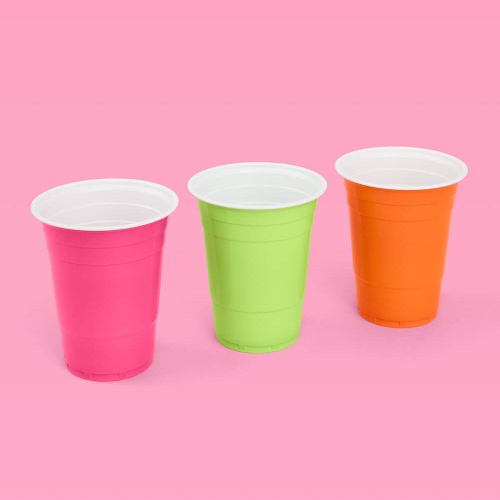 Three colorful plastic cups (pink, green, orange) on a pink background