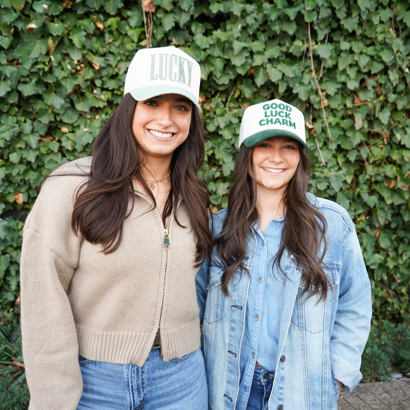 Two women wearing matching green hats with text against a green ivy wall.