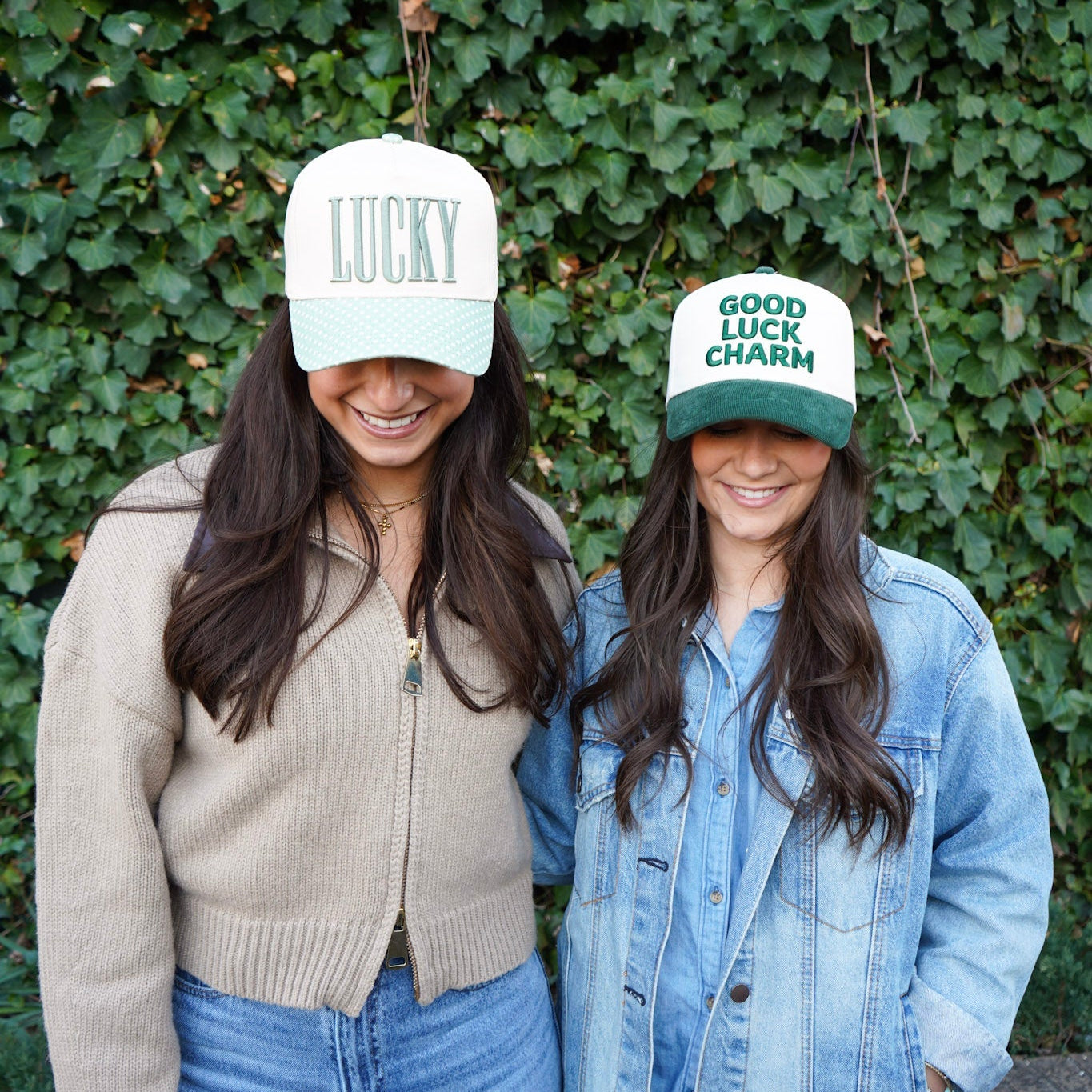 Two women wearing hats with text standing against a green ivy wall