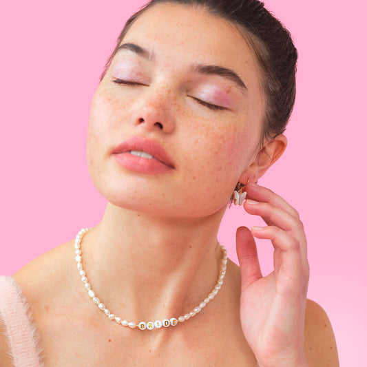 Woman wearing a pearl necklace and earrings against a pink background