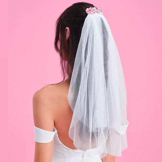 Person wearing a white wedding dress with a veil against a pink background
