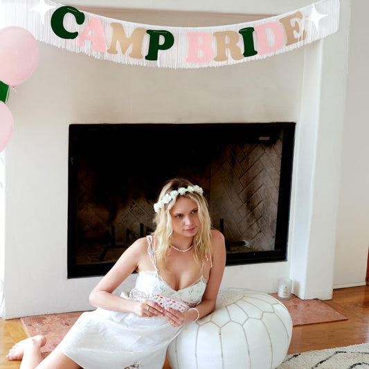 Woman in a white dress sitting on a rug with a 'Camp Bride' banner above her.