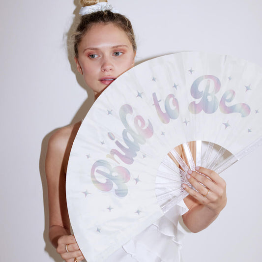 Woman holding a 'Bride to Be' fan with pastel colors against a white background