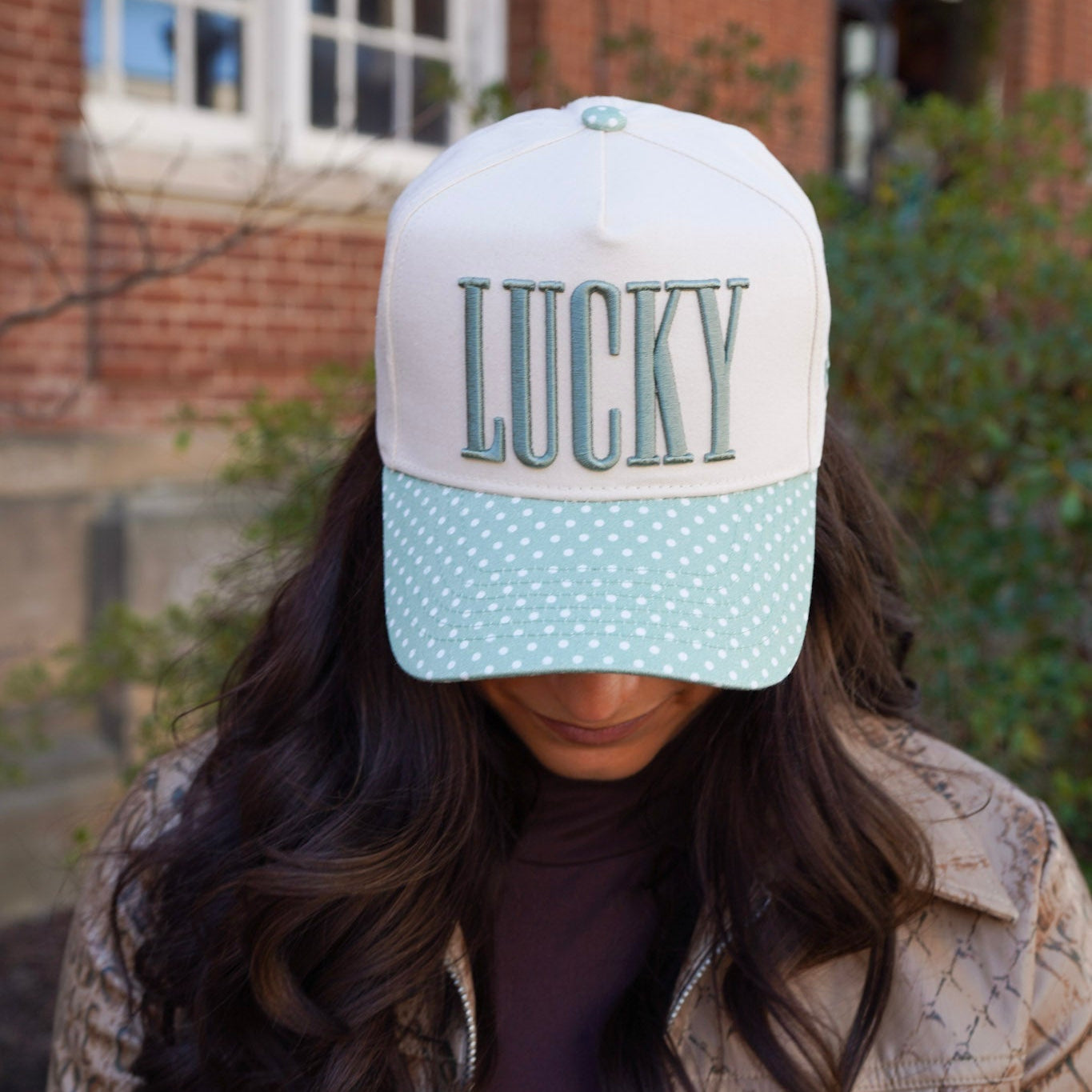 Person wearing a cap with 'LUCKY' text in front of a brick building.