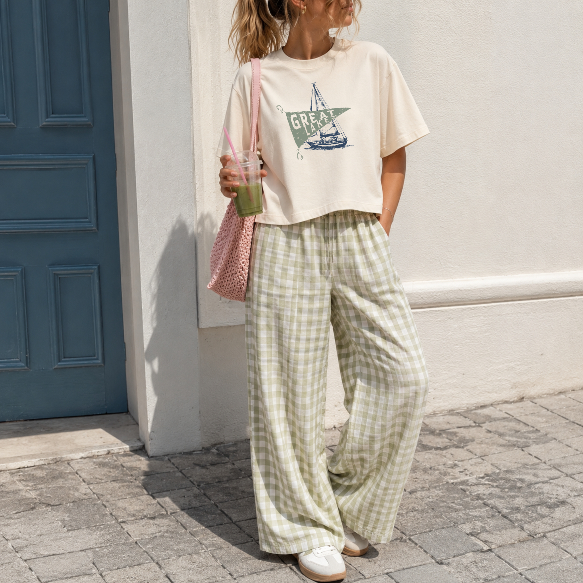 Woman wearing an ivory garment dyed boxy cropped Great Lakes graphic tee with sage gingham wide leg pants featuring a vintage sailboat and nautical pennant design.