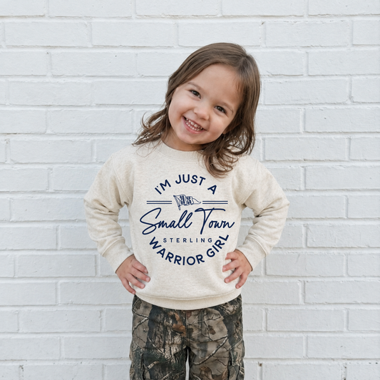 Toddler girl wearing a natural heather sweatshirt with navy I'm Just a Small Town Warrior Girl Sterling football graphic.