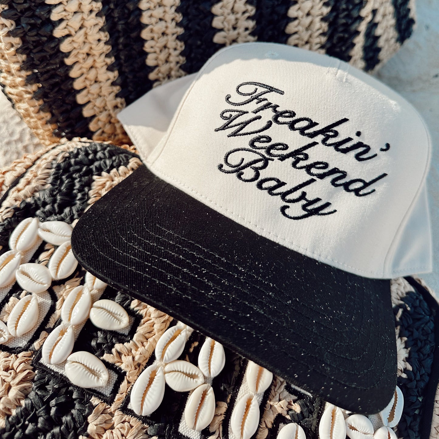White cap with black text 'Freakin' Weekend Baby' on a textured fabric background