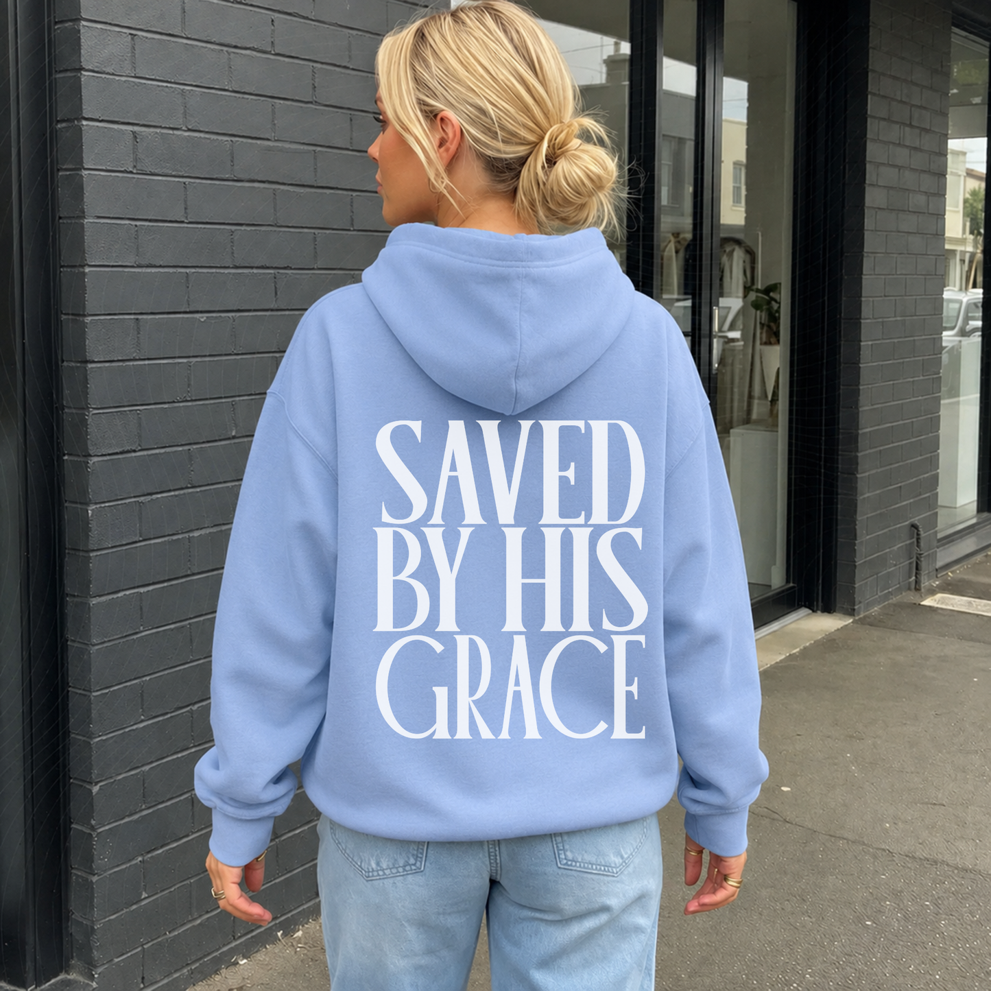 Woman wearing colony blue Saved By His Grace Christian hoodie showing oversized back faith graphic.