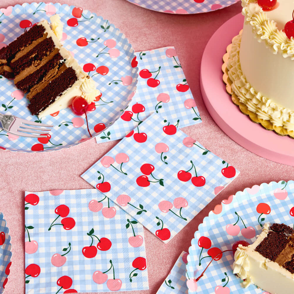 Partyware with cherry and checkered design on plates, napkins, and a cake.