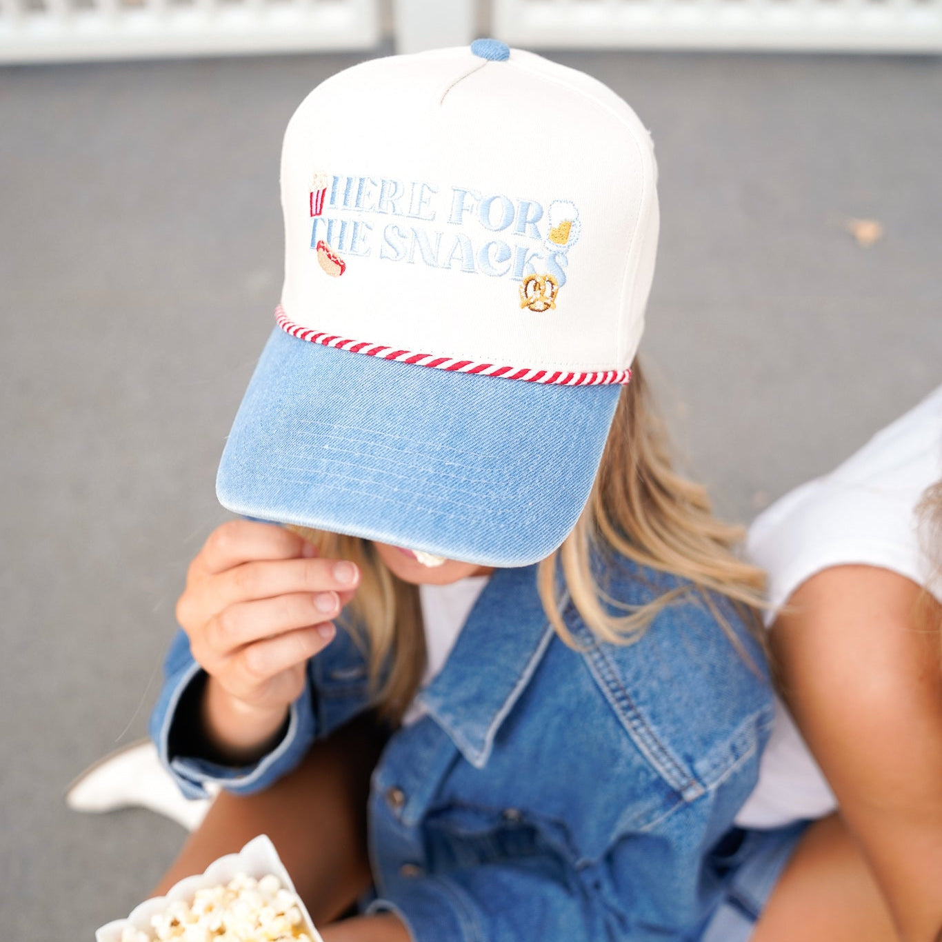 Person wearing a cap with text and graphics, holding popcorn, sitting on a bench.