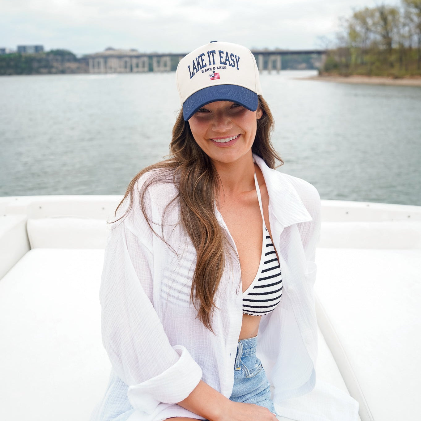 Woman wearing a 'Lake It Easy' cap sitting on a boat with a lake in the background