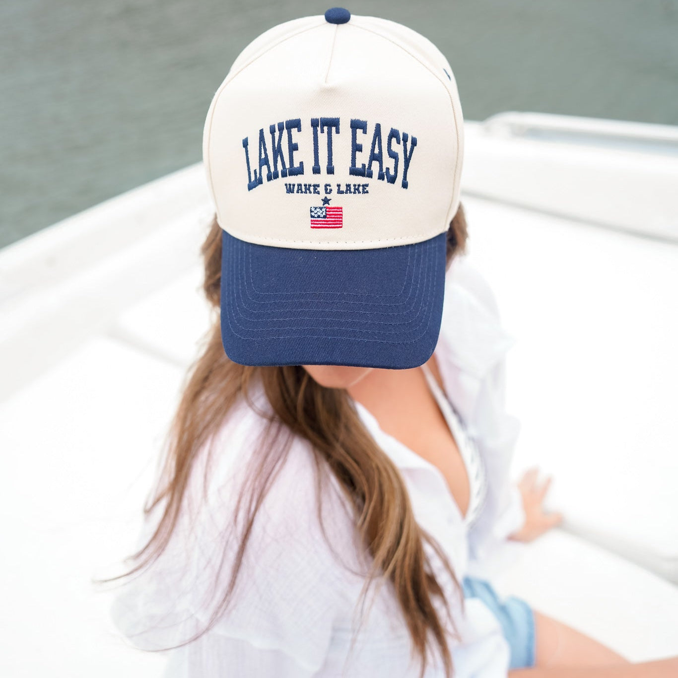 Person wearing a 'Lake It Easy' cap on a boat by a lake.