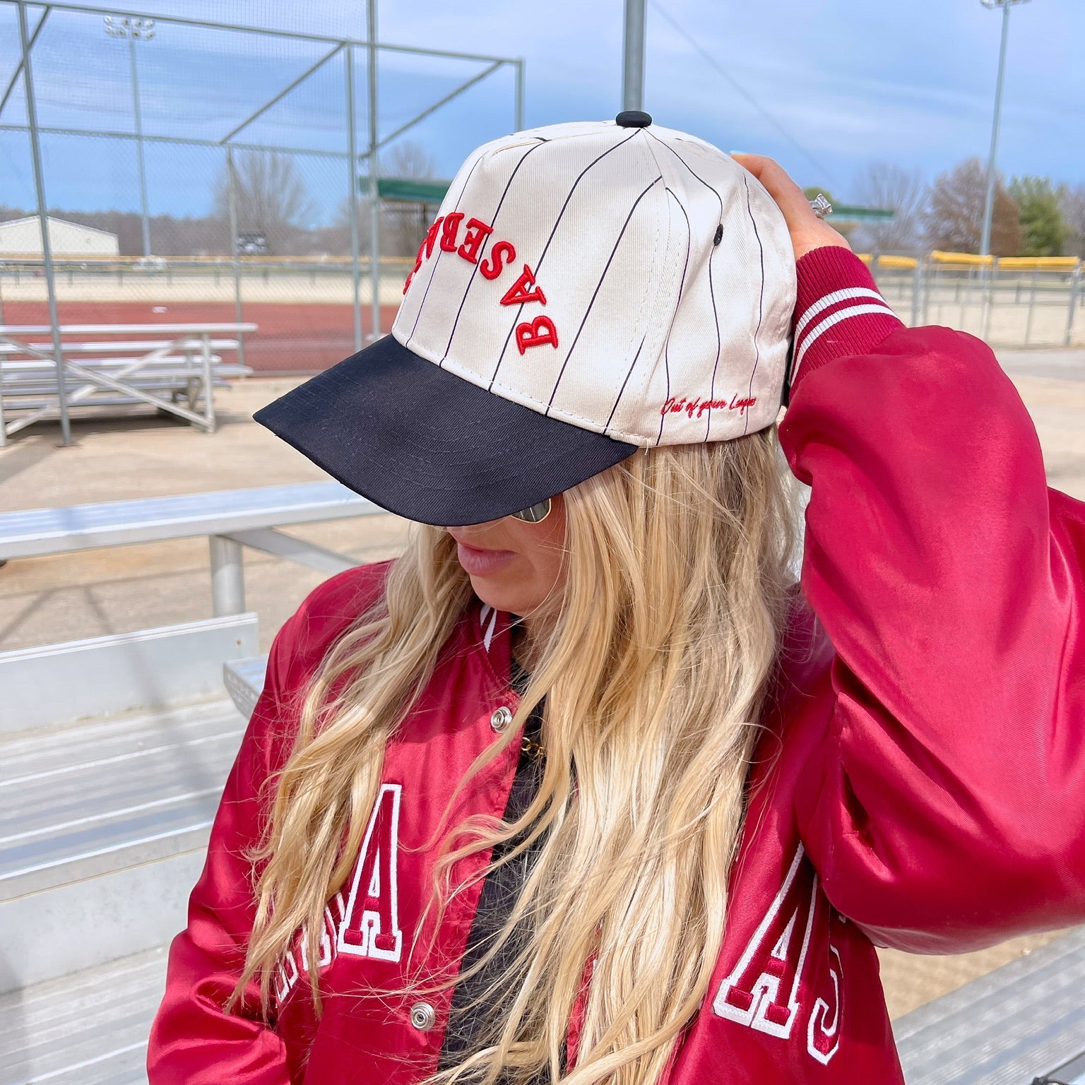 Person wearing a red letterman jacket and cap with 'A' logo, standing in a sports field.
