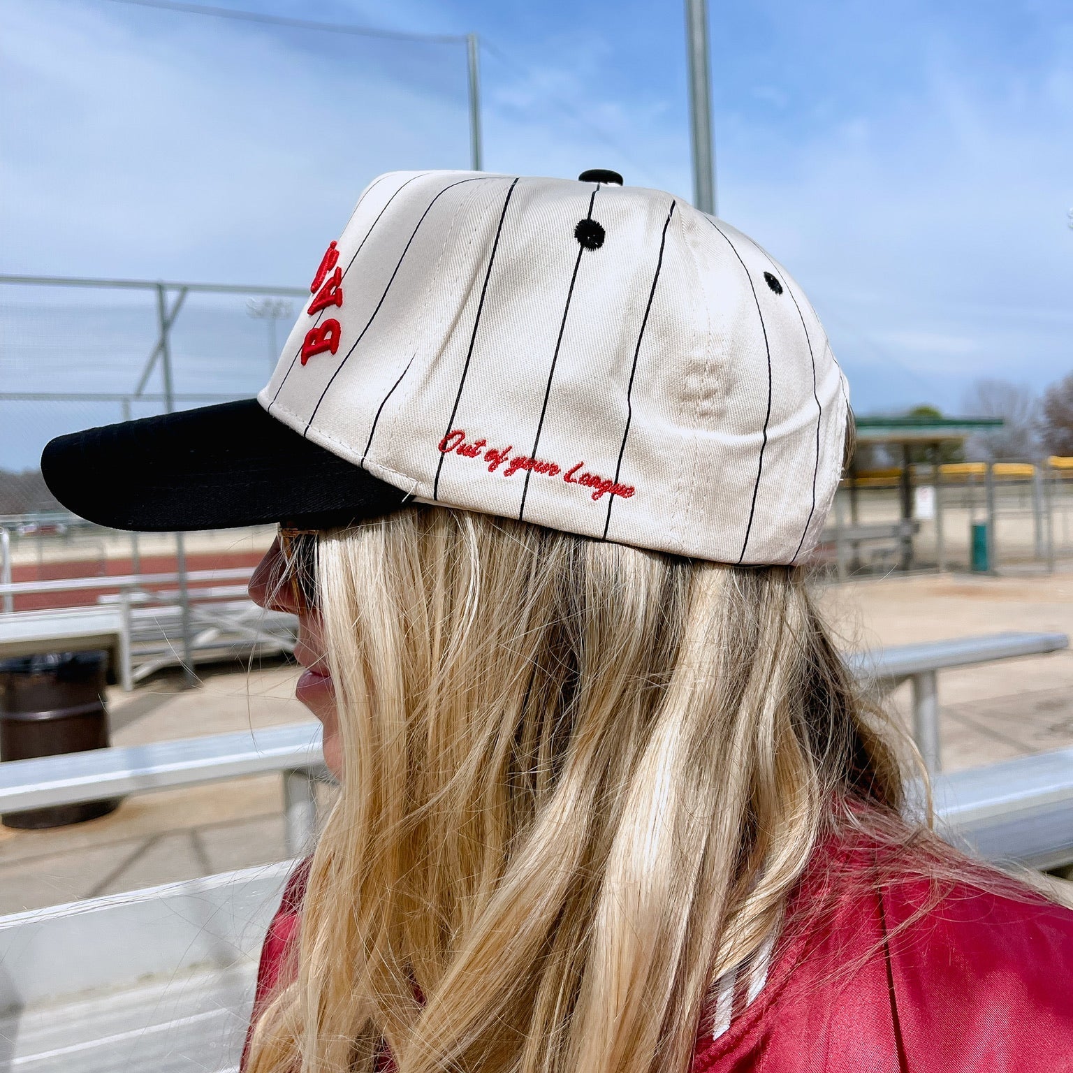 Person wearing a cap with text, sitting outdoors on bleachers.