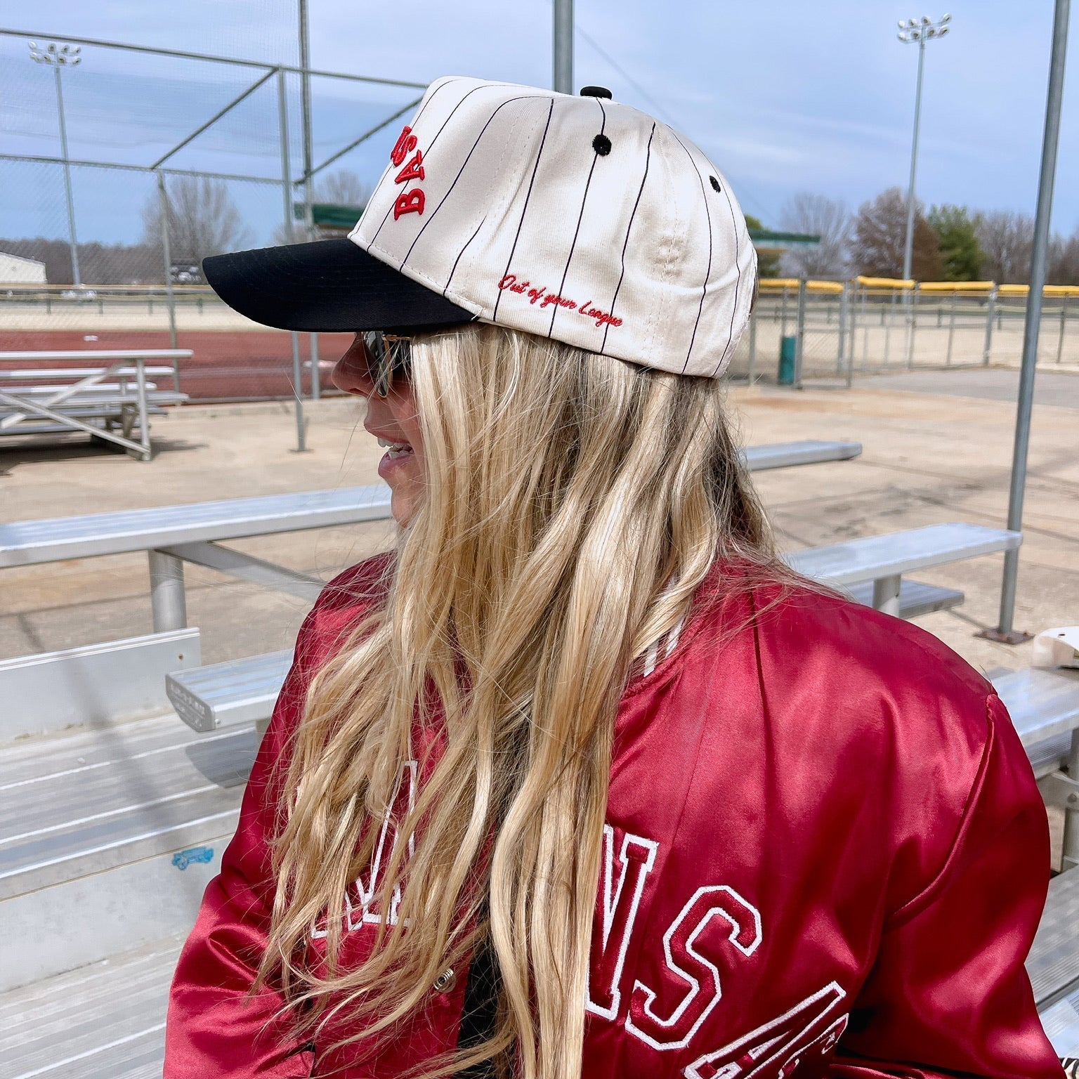 Person wearing a red letterman jacket and cap with 'Base' text, standing outdoors.