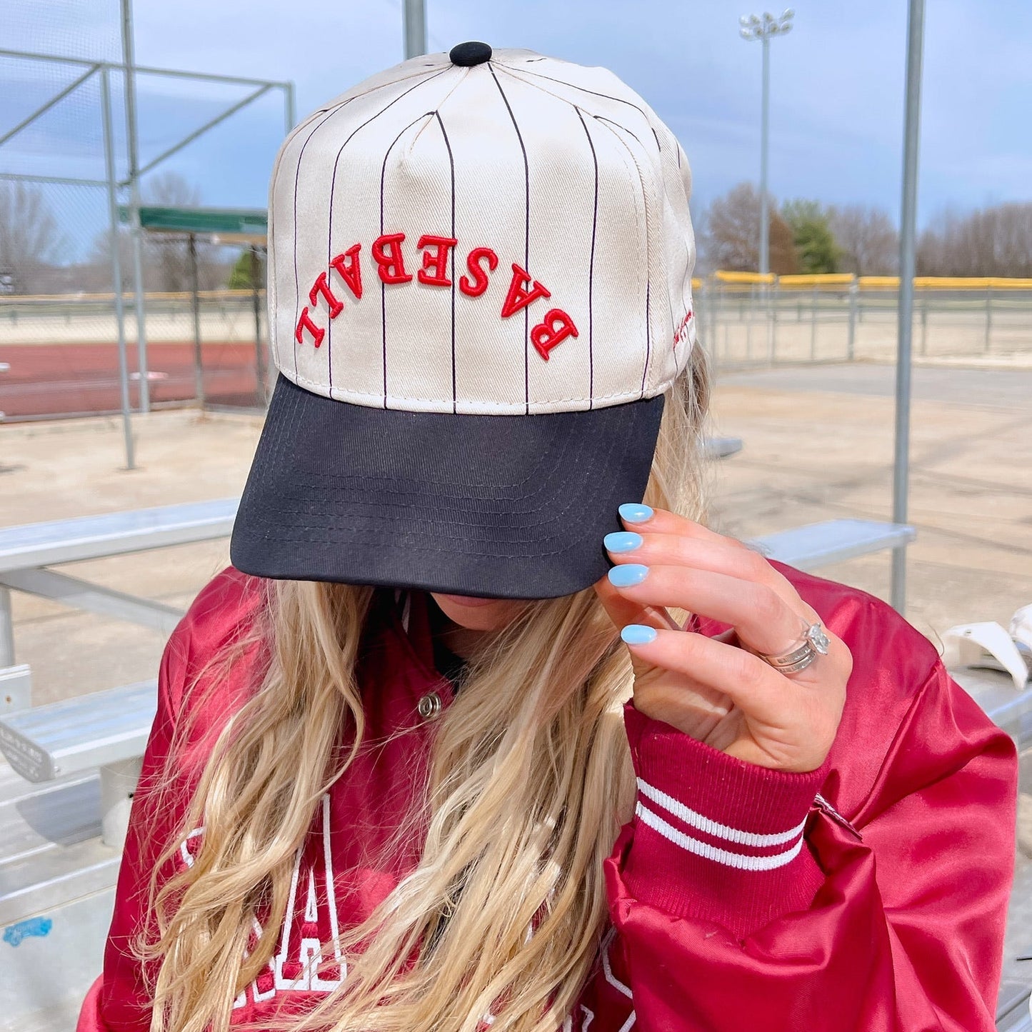 Person wearing a red jacket and a cap with 'BASEBALL' text at a sports field.