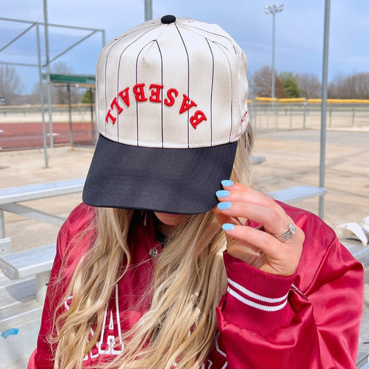 Person wearing a red jacket and a cap with 'BASEBALL' text at a sports field.