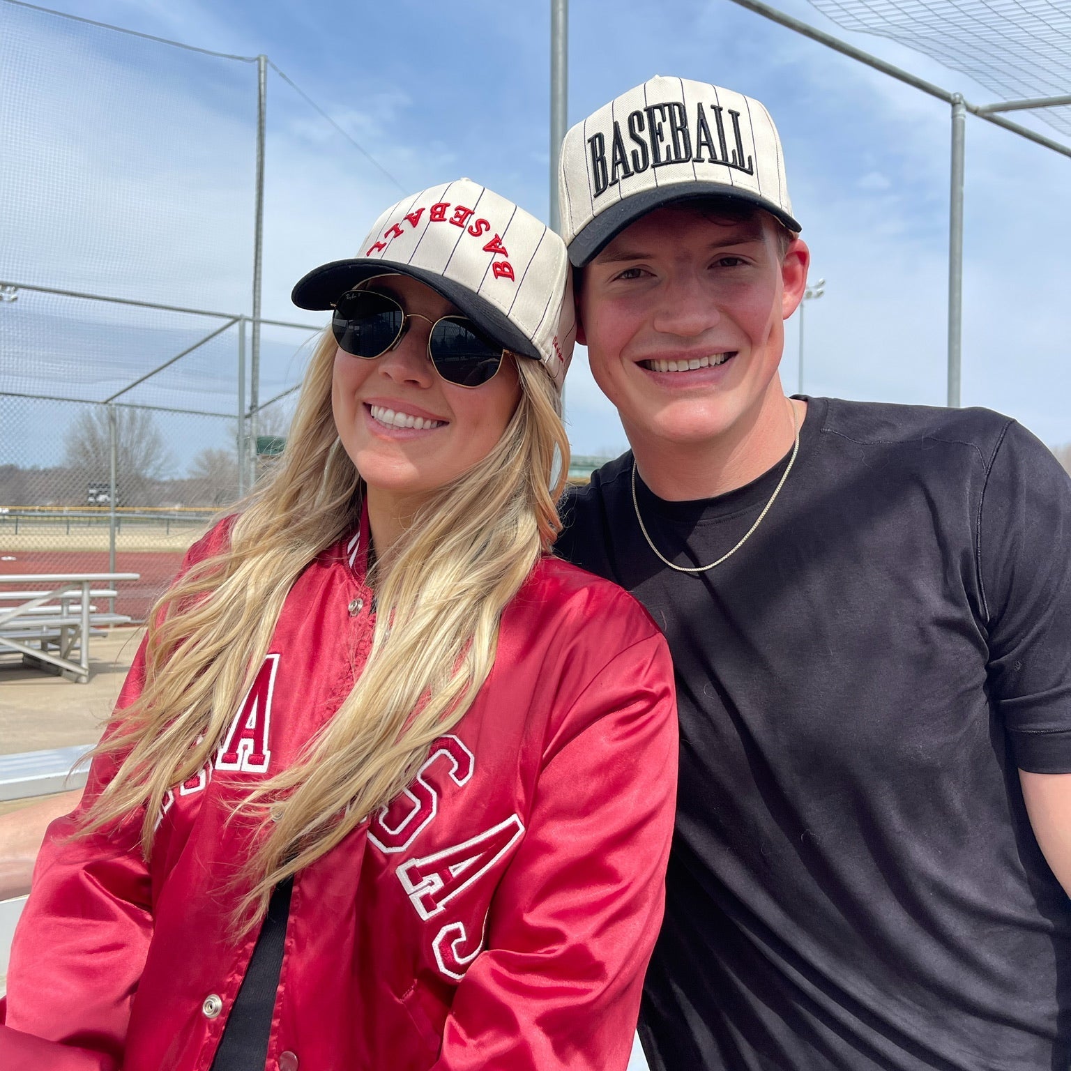 Two people wearing baseball caps and posing outdoors with a clear sky.