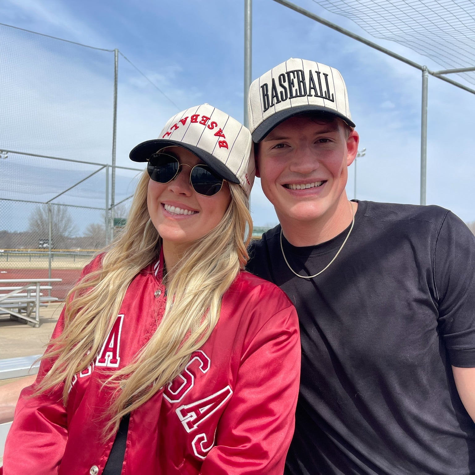 Two people wearing baseball caps and posing outdoors with a clear sky.