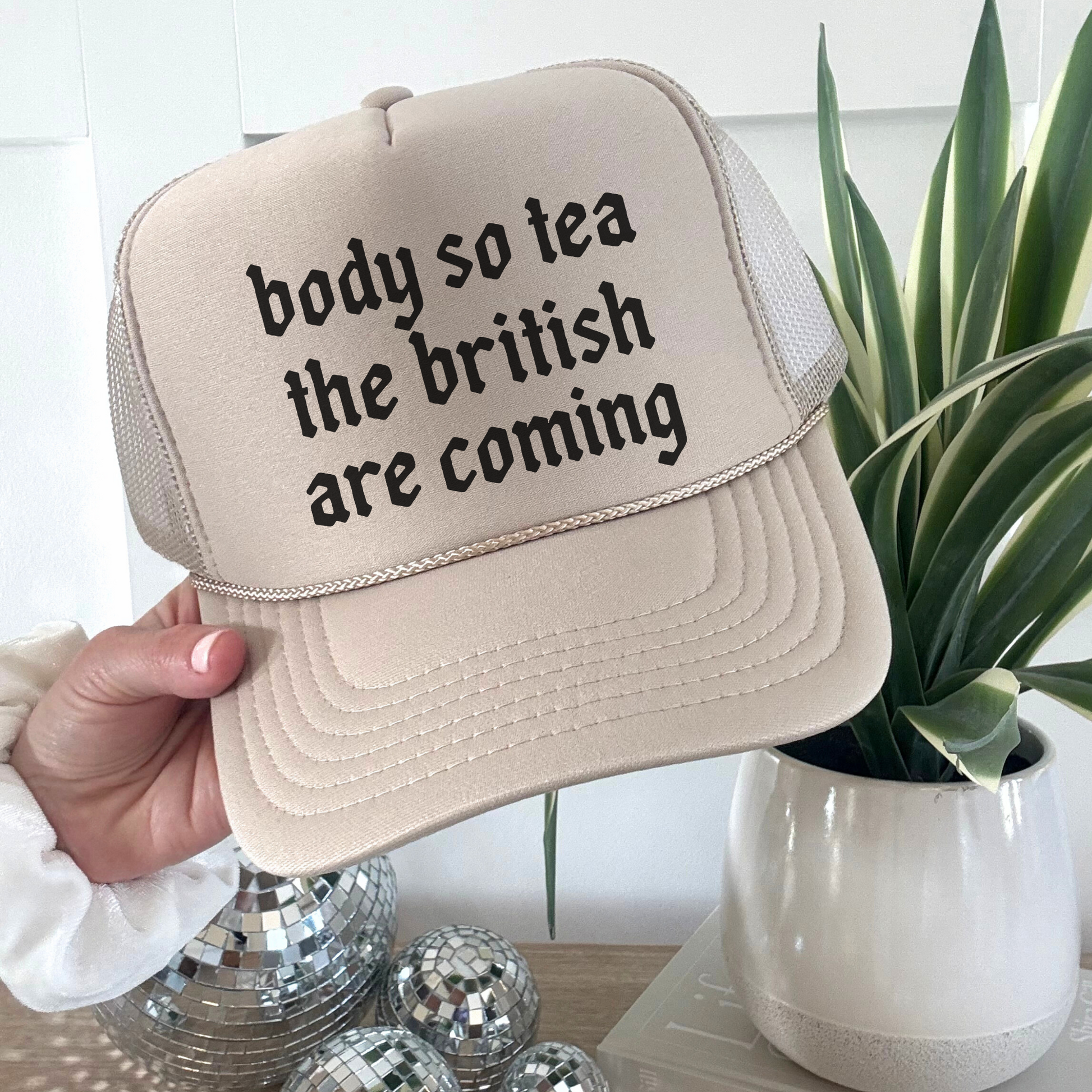 Beige foam front trucker hat with “body so tea the british are coming” printed text