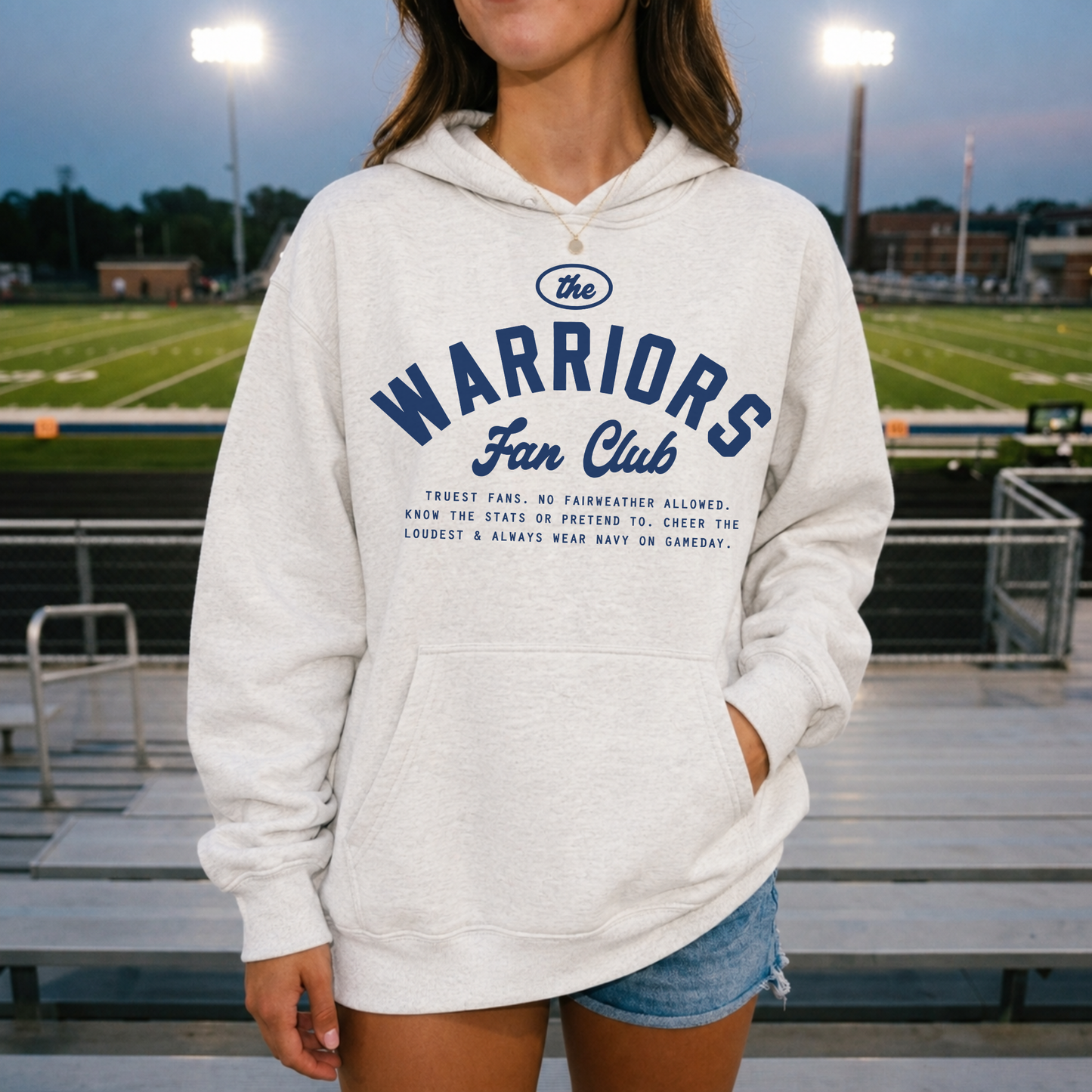 Woman wearing a premium oatmeal heather Sterling Warriors Fan Club hoodie at Roscoe Eades Stadium during football season.