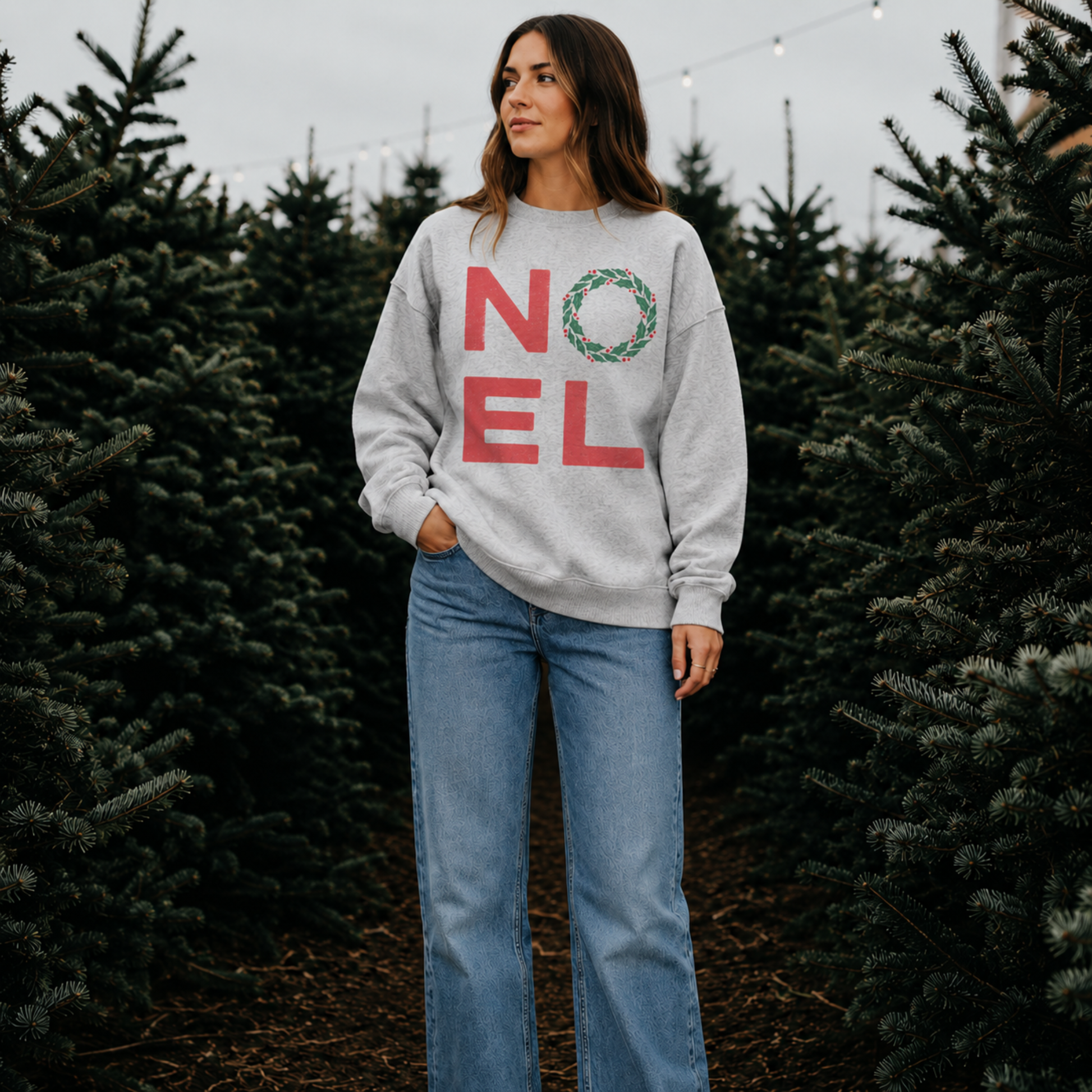Woman wearing an oatmeal heather NOEL Christmas sweatshirt at a Christmas tree farm.